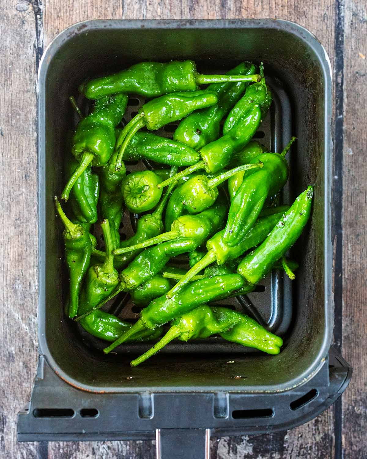 An air fryer basket with oil and seasoning coated peppers in it.