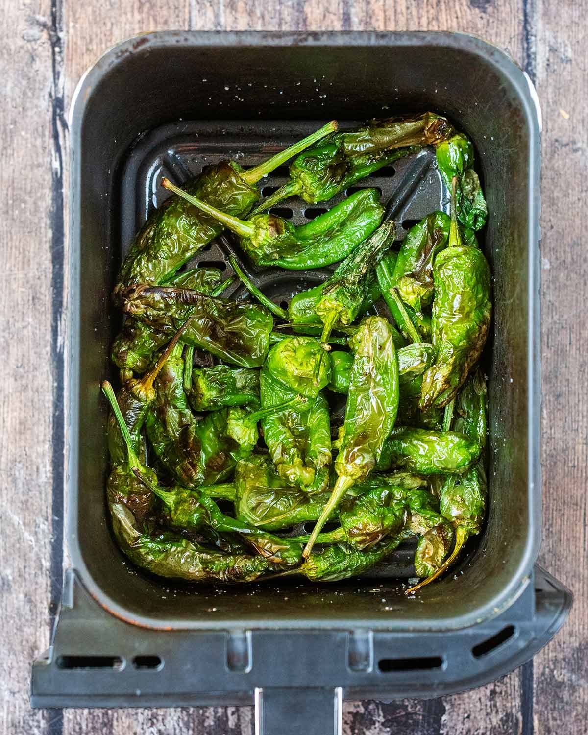 Cooked padron peppers in an air fryer basket.