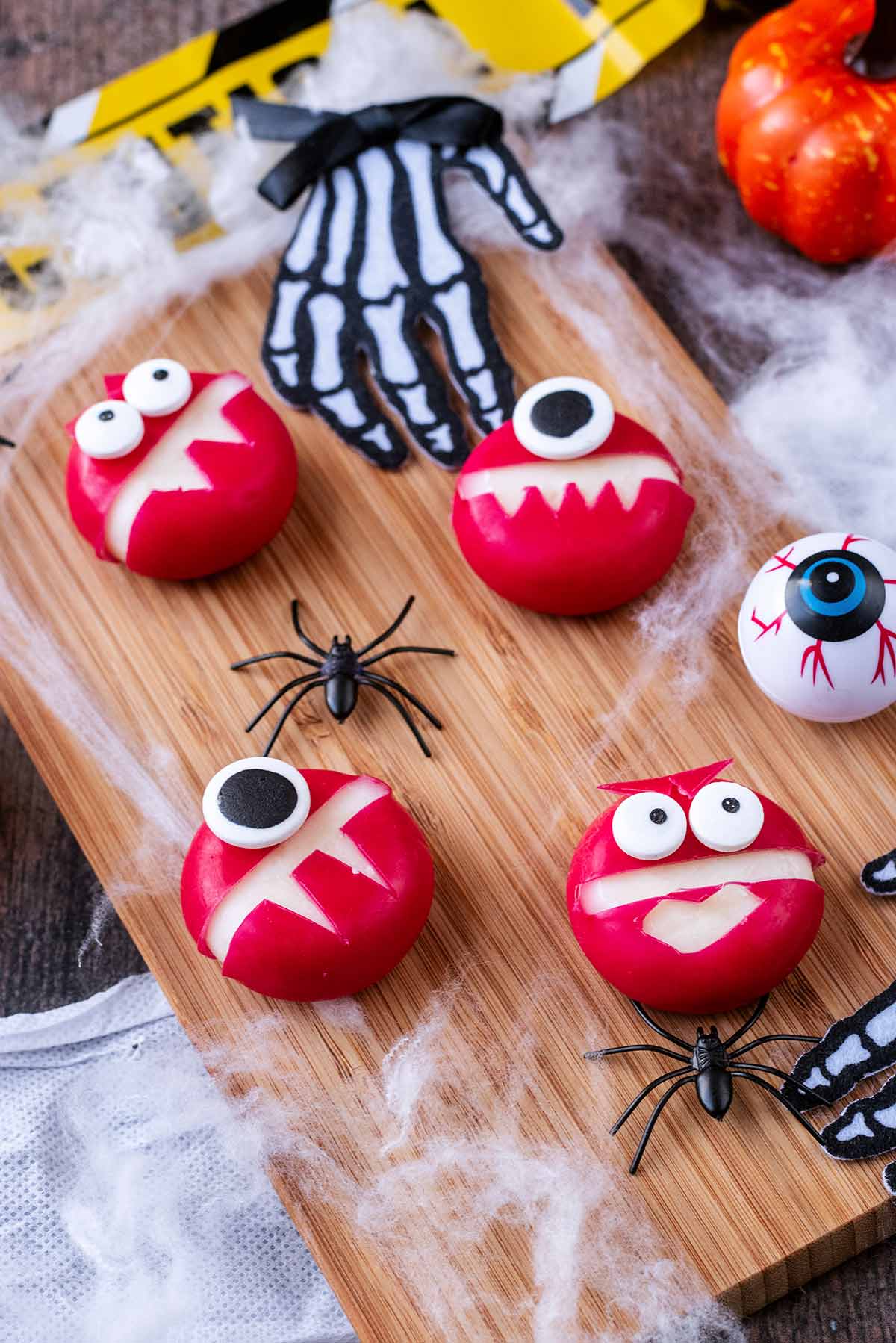 Babybel monsters on a wooden board with cobwebs and fake skeleton hands.