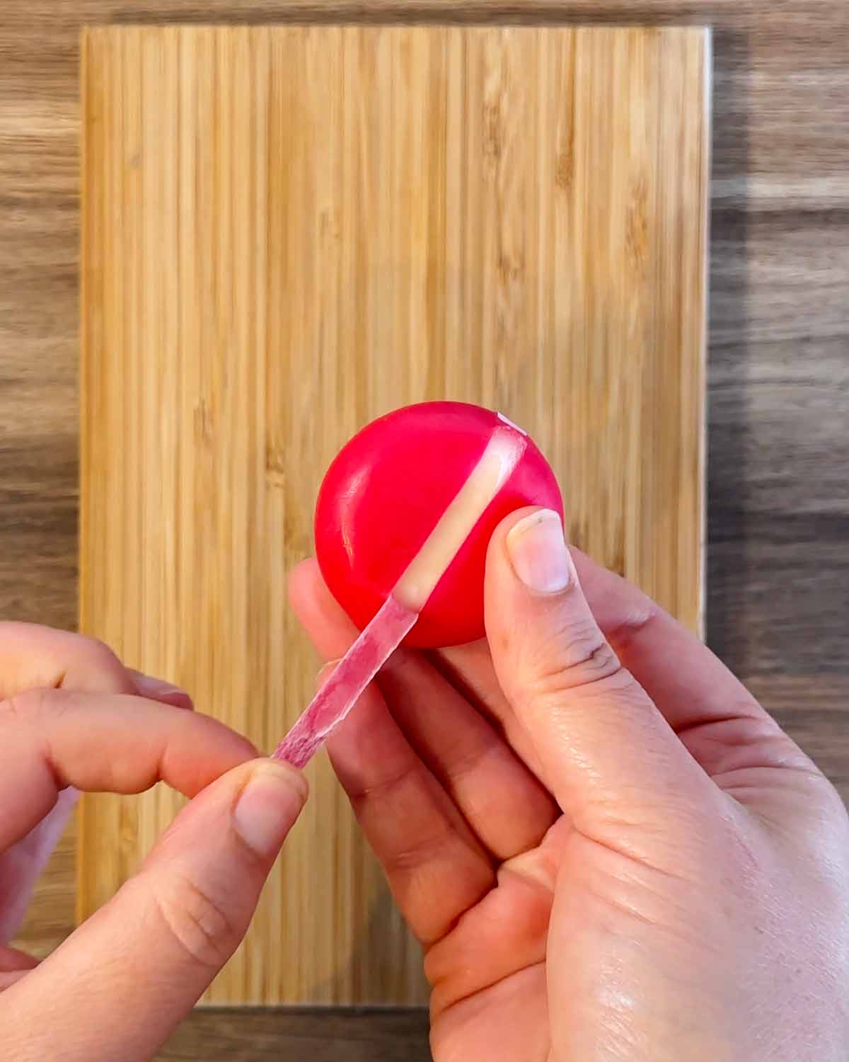 A hand peeling wax off of a Babybel cheese.