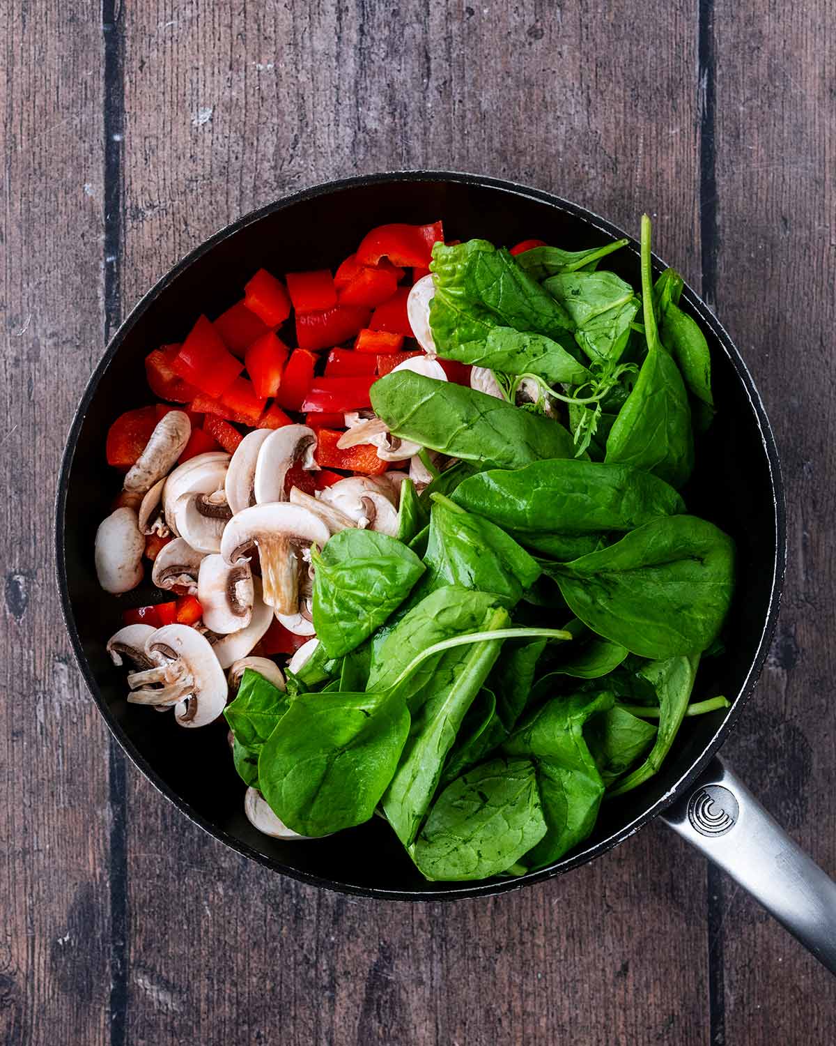 A saucepan with red pepper, spinach and mushrooms cooking in it.