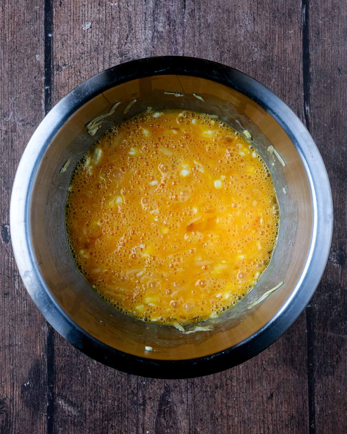 A mixing bowl containing a mixture of whisked egg and cheese.