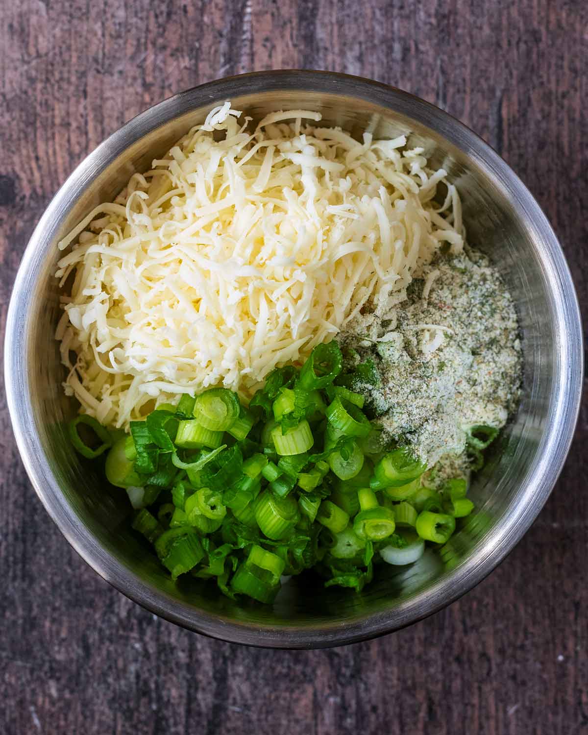 A mixing bowl containing yogurt, cheese, spring onions and ranch seasoning.