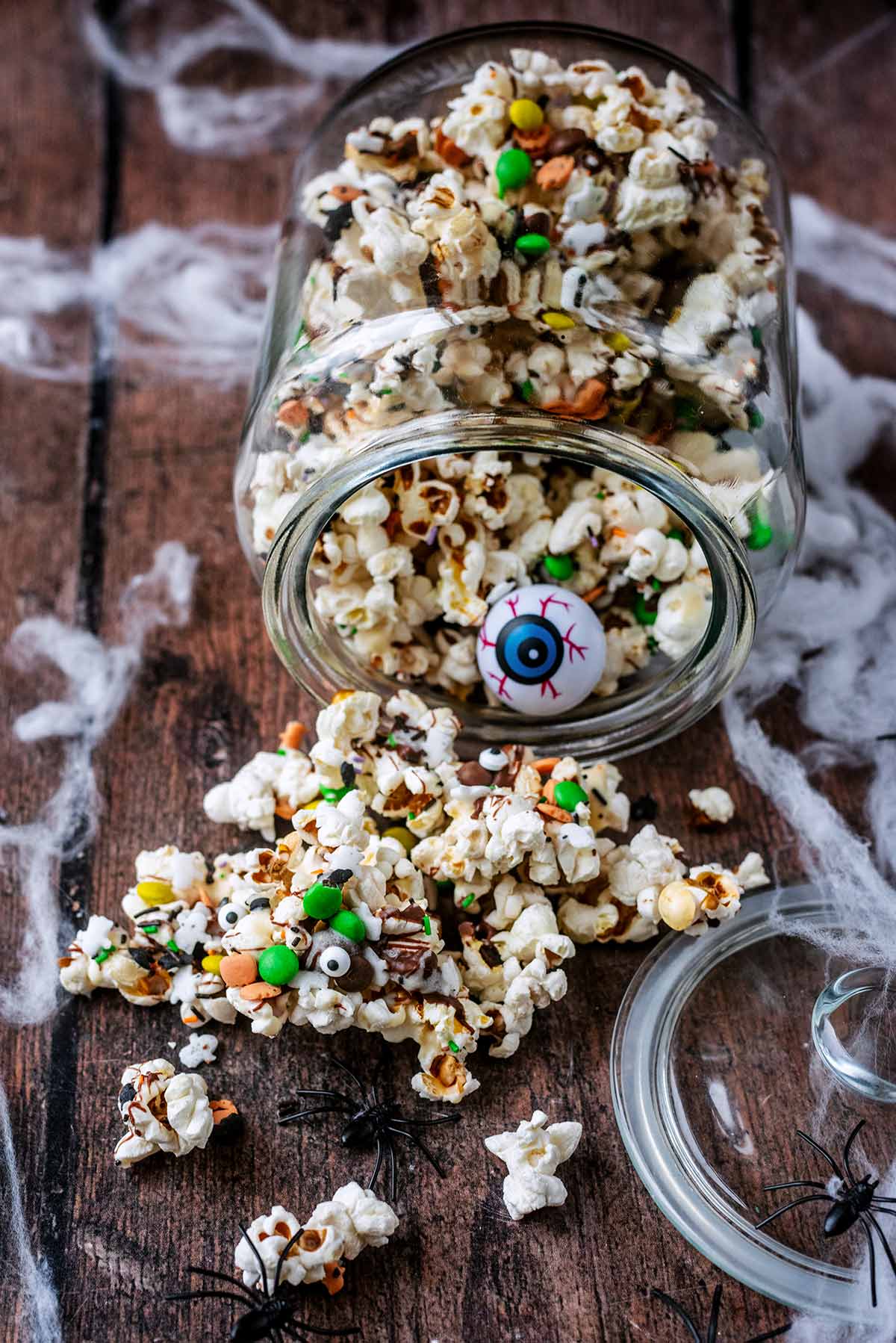 A jar of popcorn that has fallen over and popcorn has spilled out.