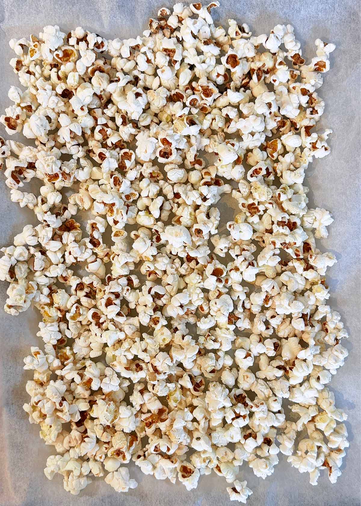 Popcorn spread over a lined baking sheet.