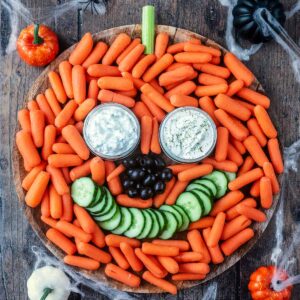 A Halloween veggie tray surrounded by cobwebs and small plastic pumpkins.