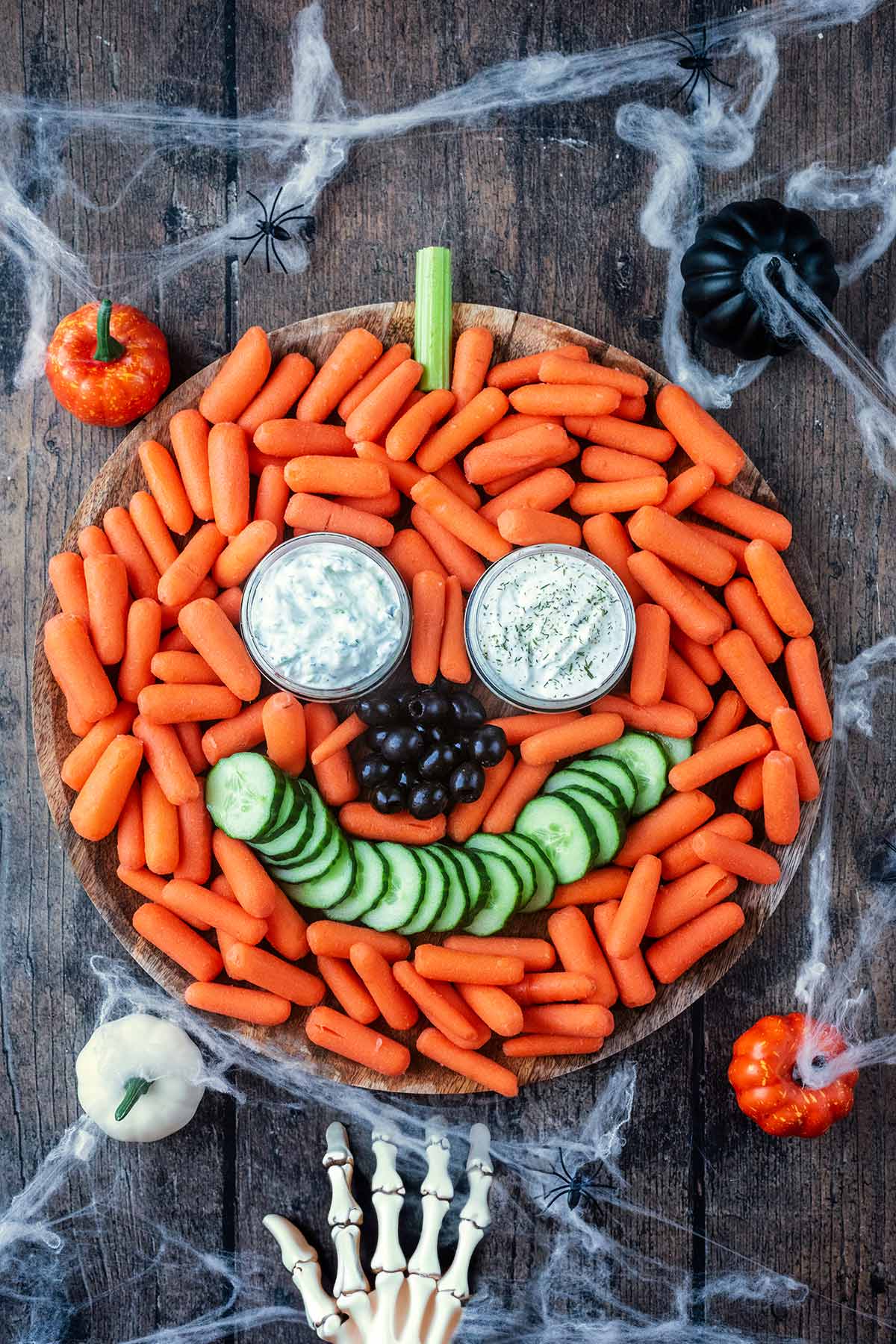 Carrots arranged into a pumpkin shape with dips for eyes olives for a nose and cucumber for a mouth.