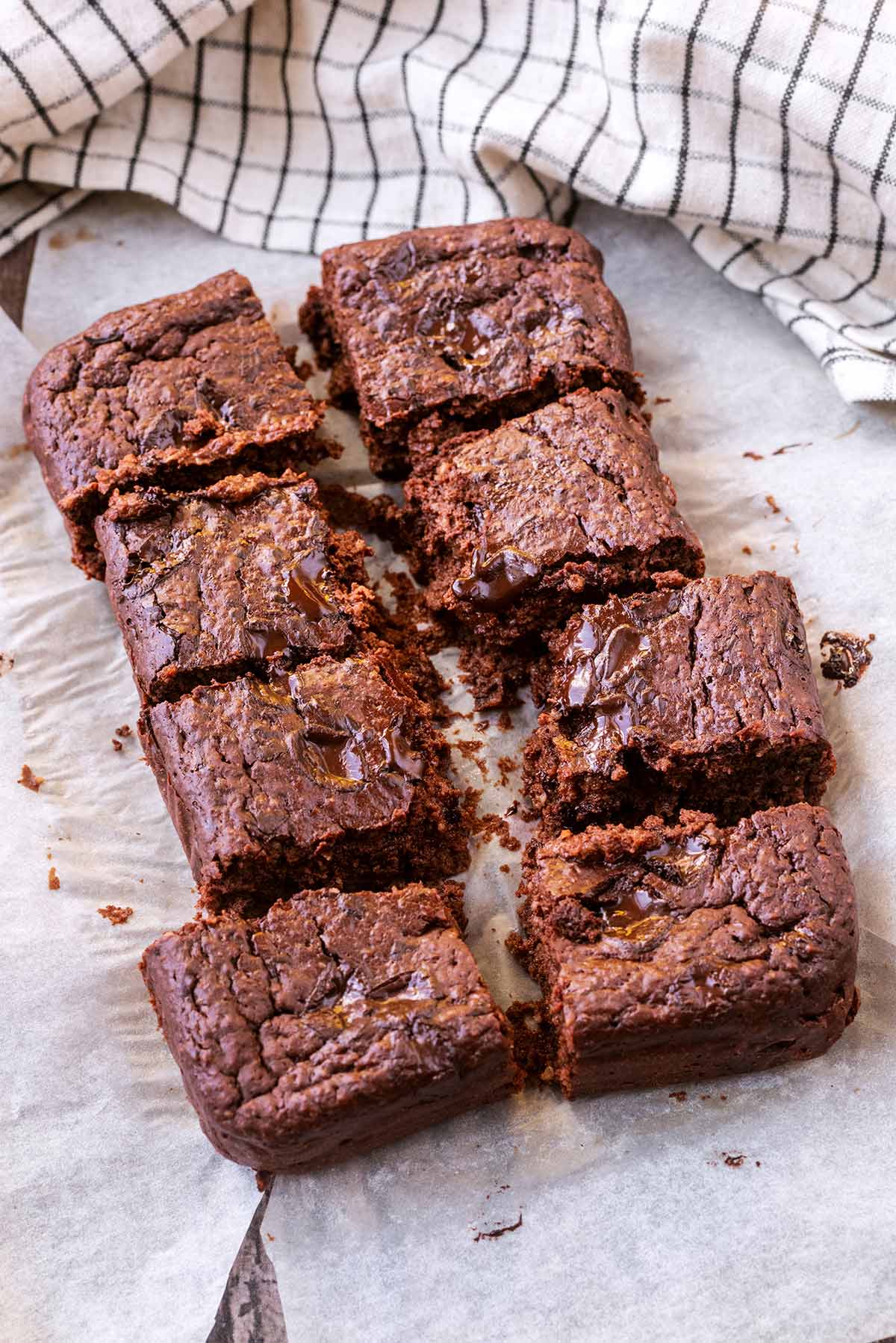 Eight square chocolate brownies on a sheet of parchment paper.