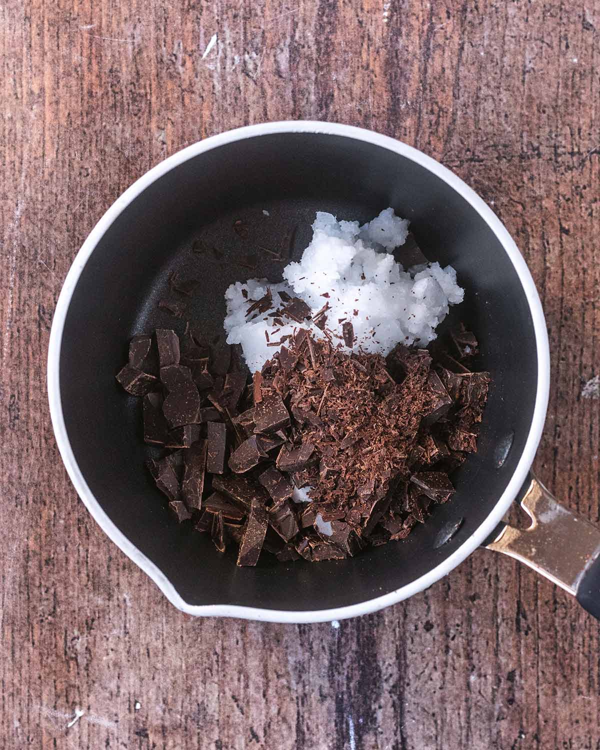 A saucepan containing chopped chocolate and coconut oil.