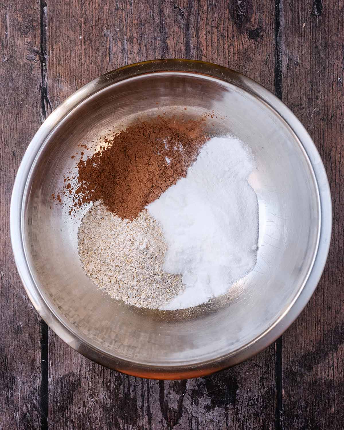 A mixing bowl containing oat flour, granulated sweetener and cocoa powder.