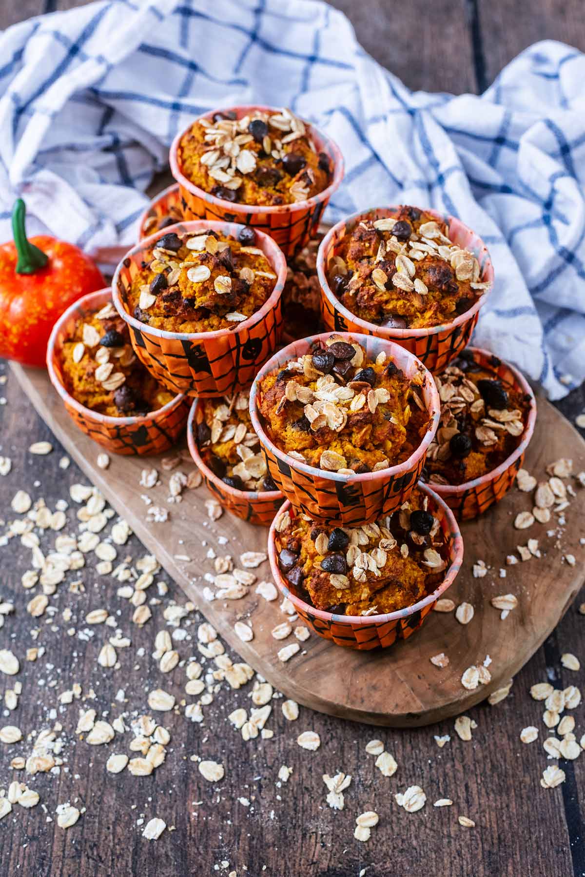 Pumpkin chocolate chip muffins on a wooden serving board surrounded by oats.