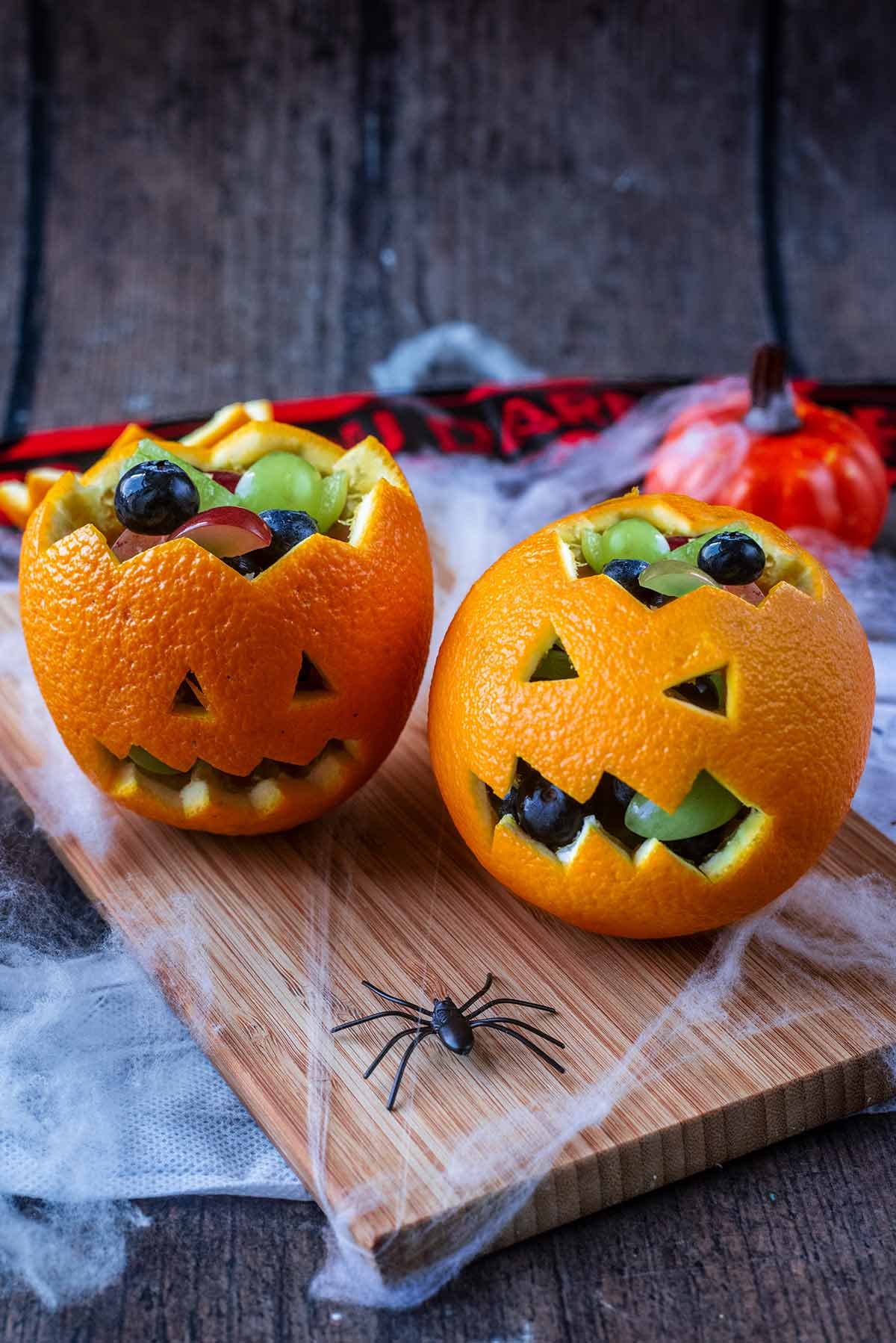 Two oranges cut into Jack O'Lantern designs, on a wooden board.