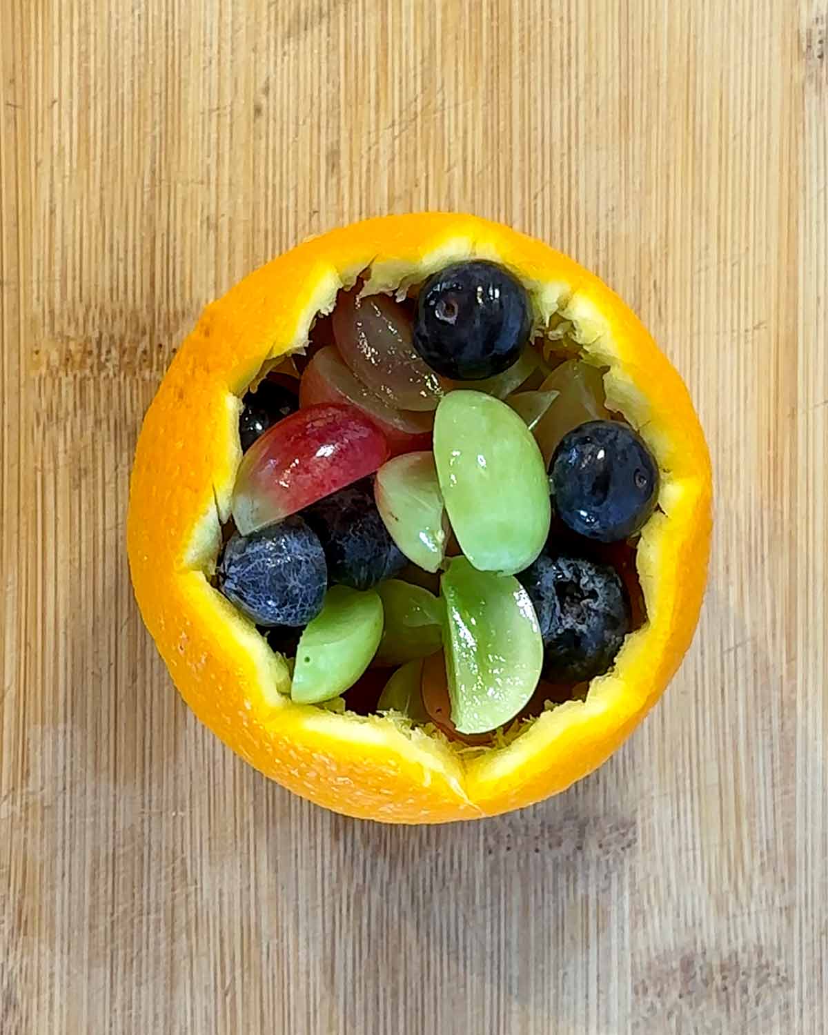 The orange skin filled with cut grapes and blueberries.