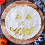 A Jack O'Lantern Quesadilla on a round wooden board.