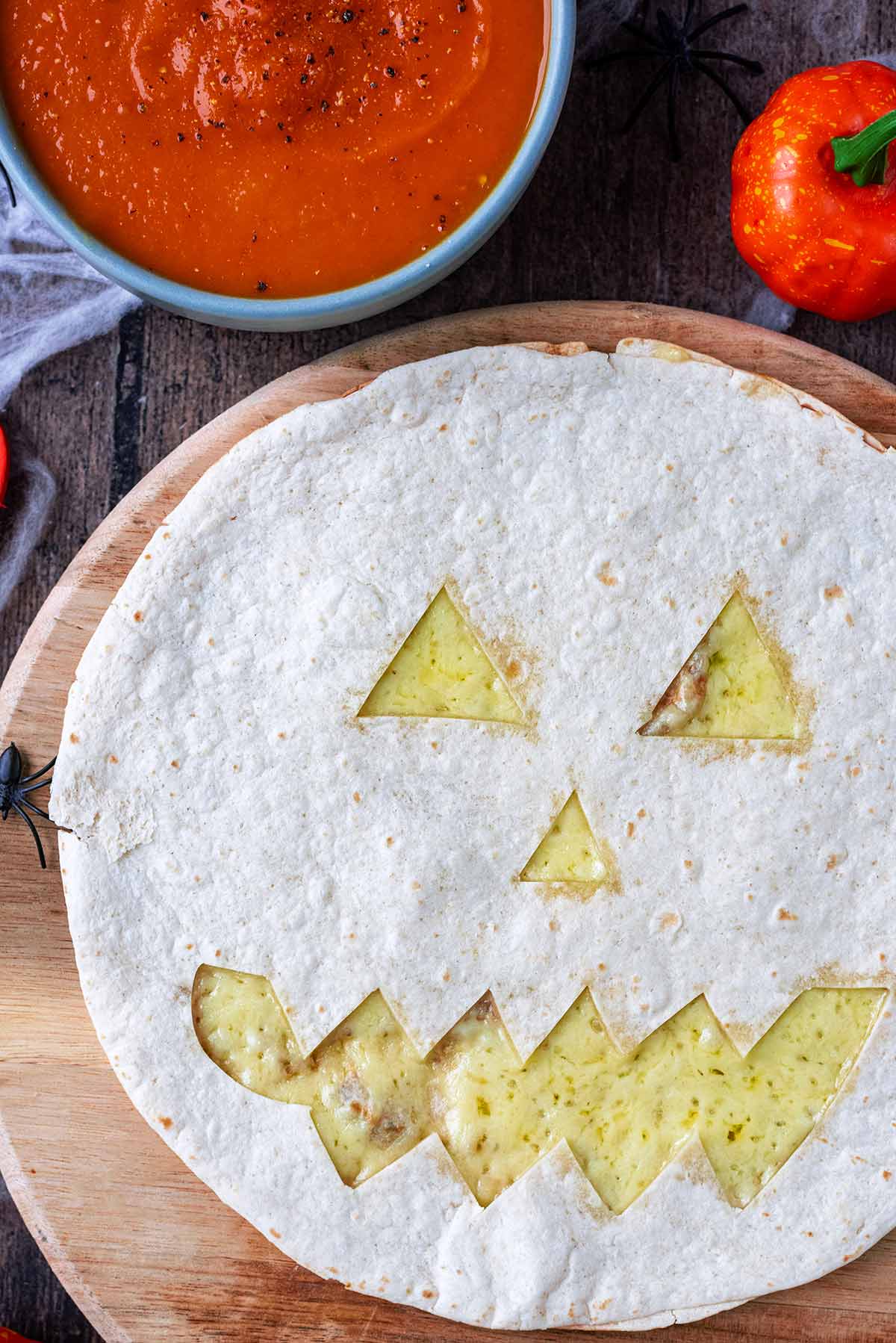 A pumpkin shaped quesadilla next to a bowl of tomato soup.