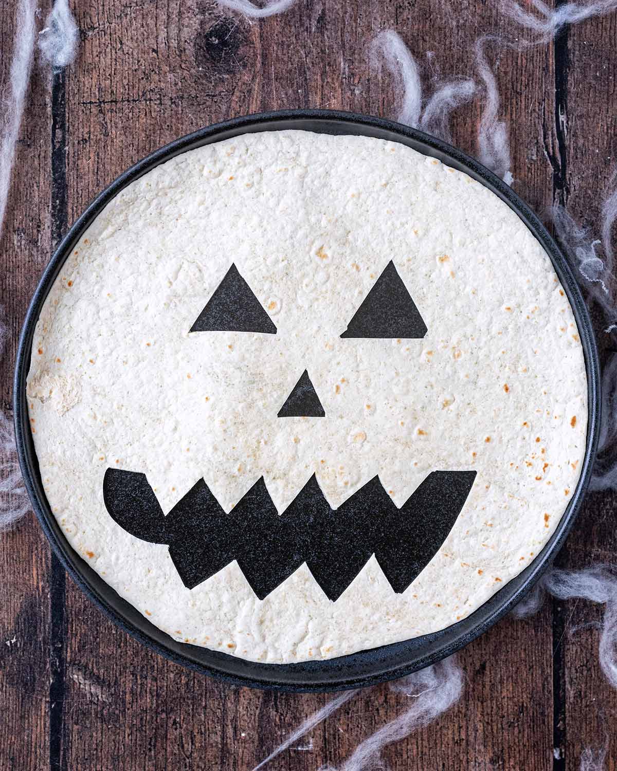 A flour tortilla with a Jack O'Lantern face cut into it.