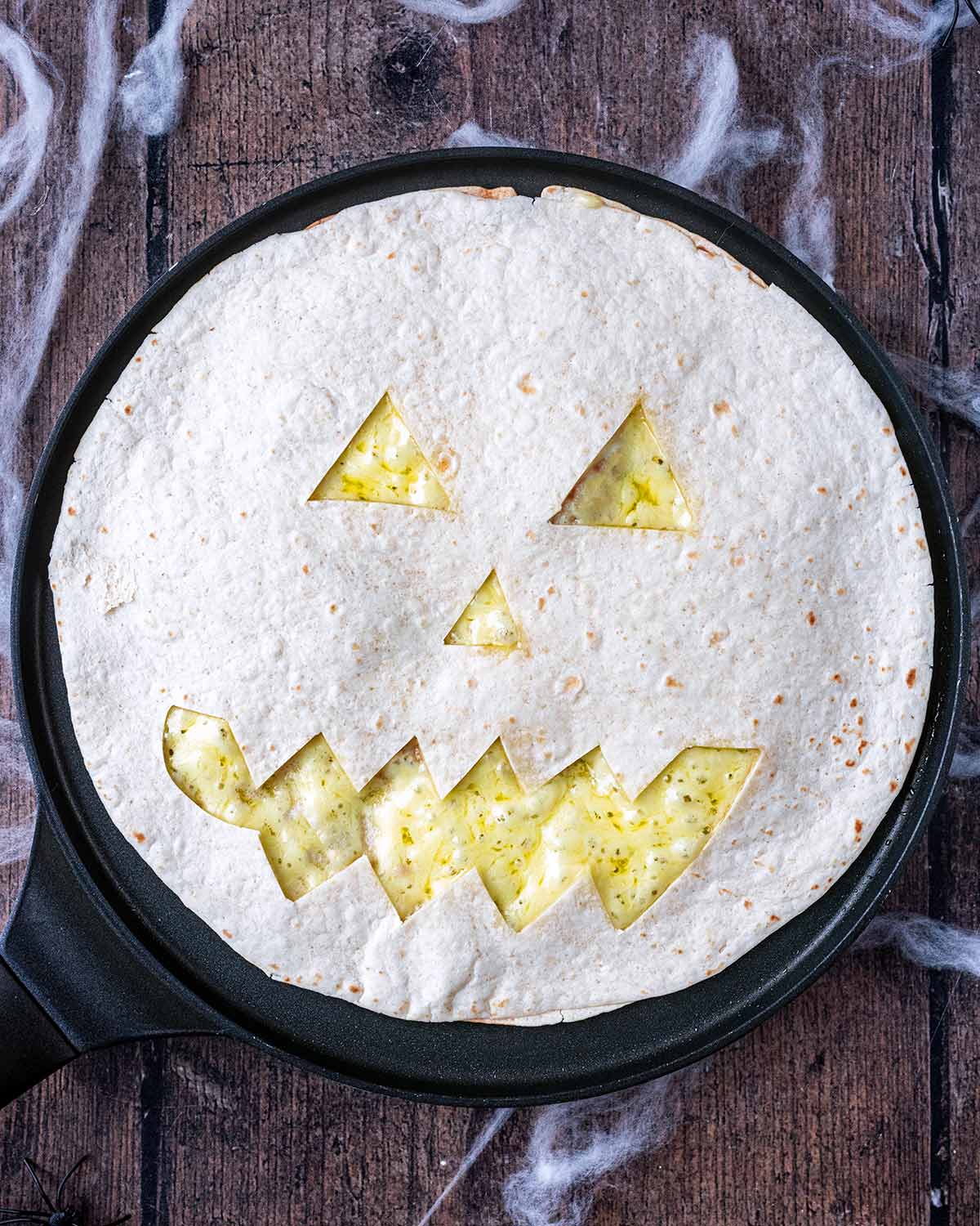 Melted cheese showing through the Jack O'Lantern tortilla face.