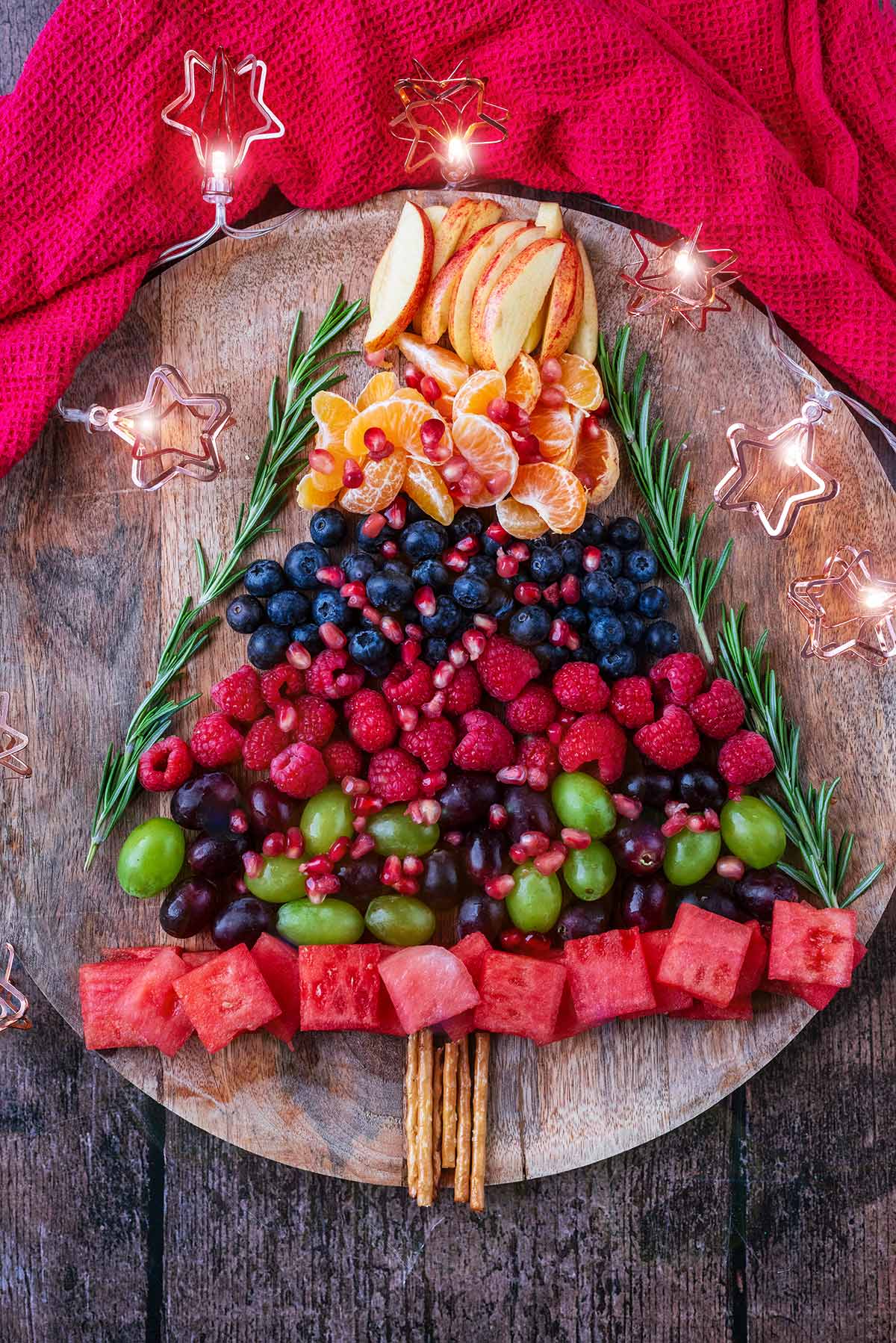 Various fruits and berries shaped into a Christmas tree surrounded by fairy lights.