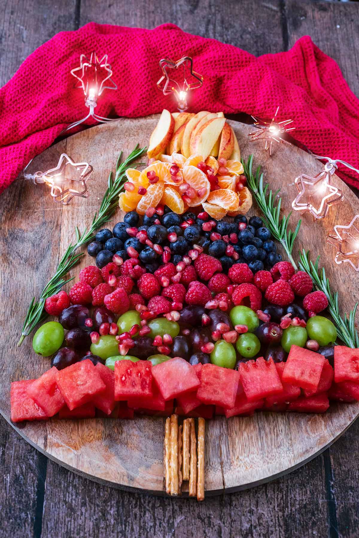 A Christmas tree shaped fruit platter in front of a red towel.