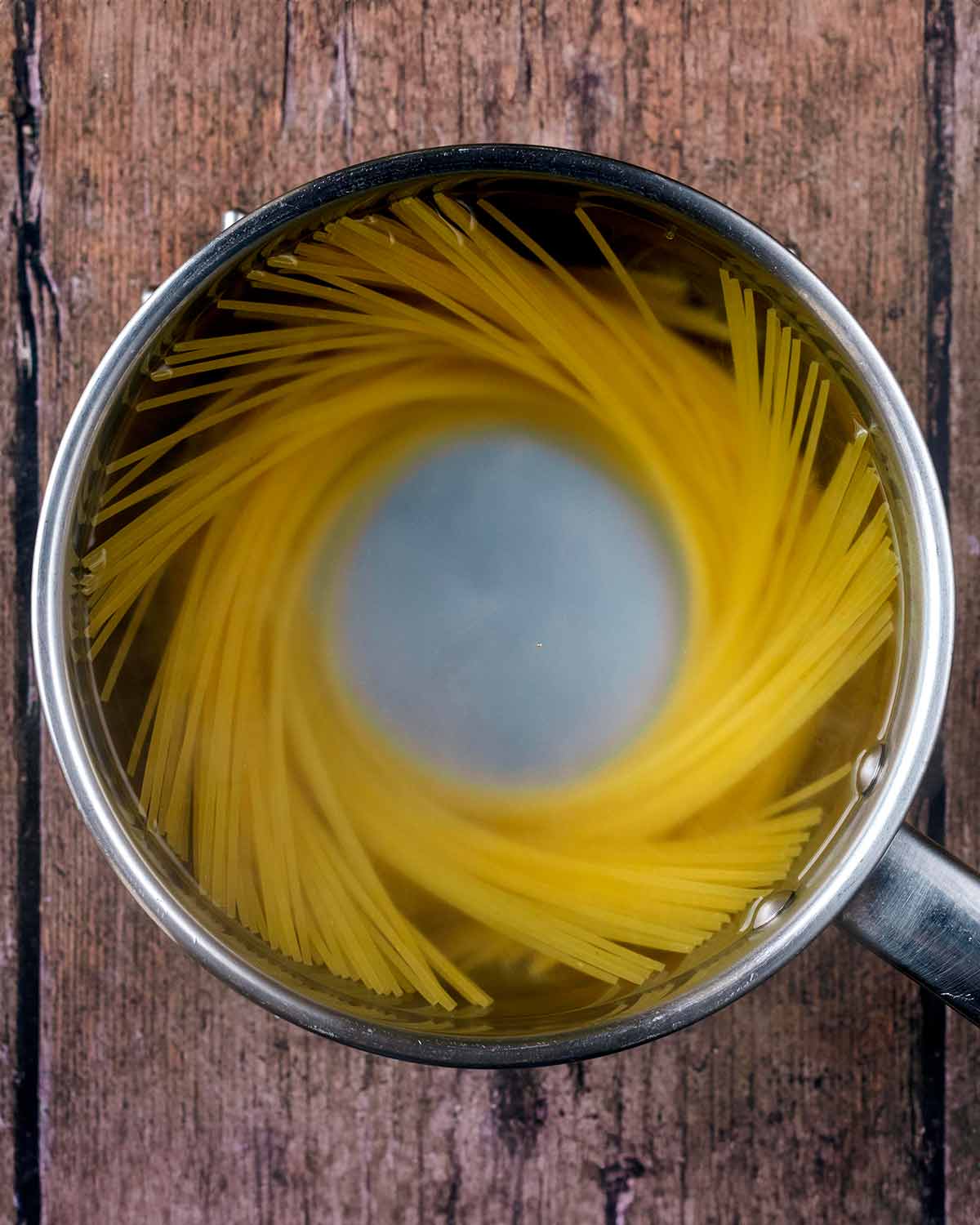 A saucepan with spaghetti cooking in it.