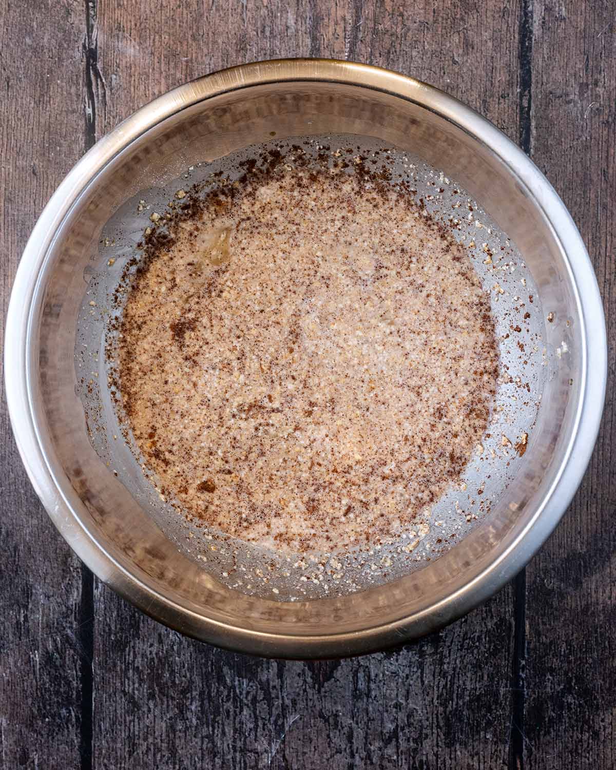 Oats, spices and milk mixed together in a metal bowl.