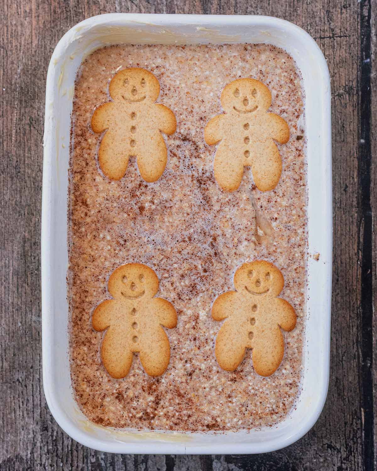 Gingerbread oat mixture poured into a baking dish with four gingerbread people on top.