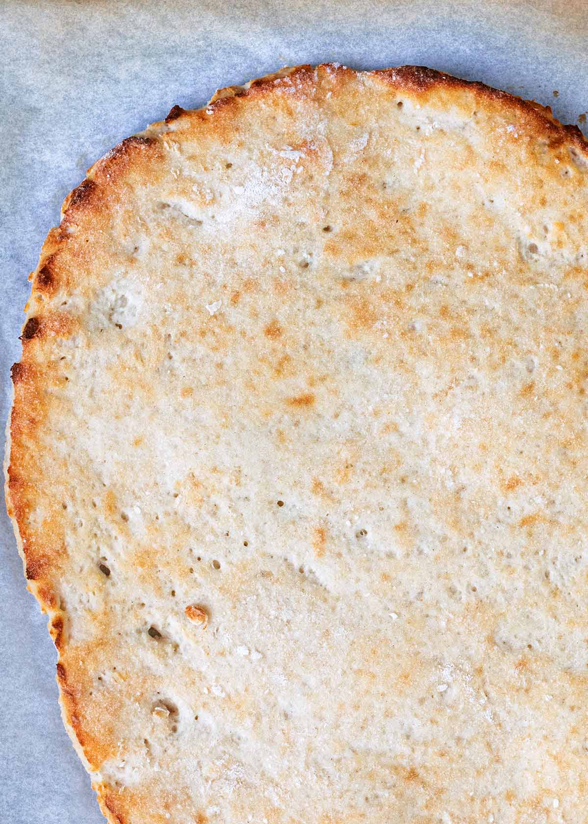 A pizza crust on a sheet of baking paper.