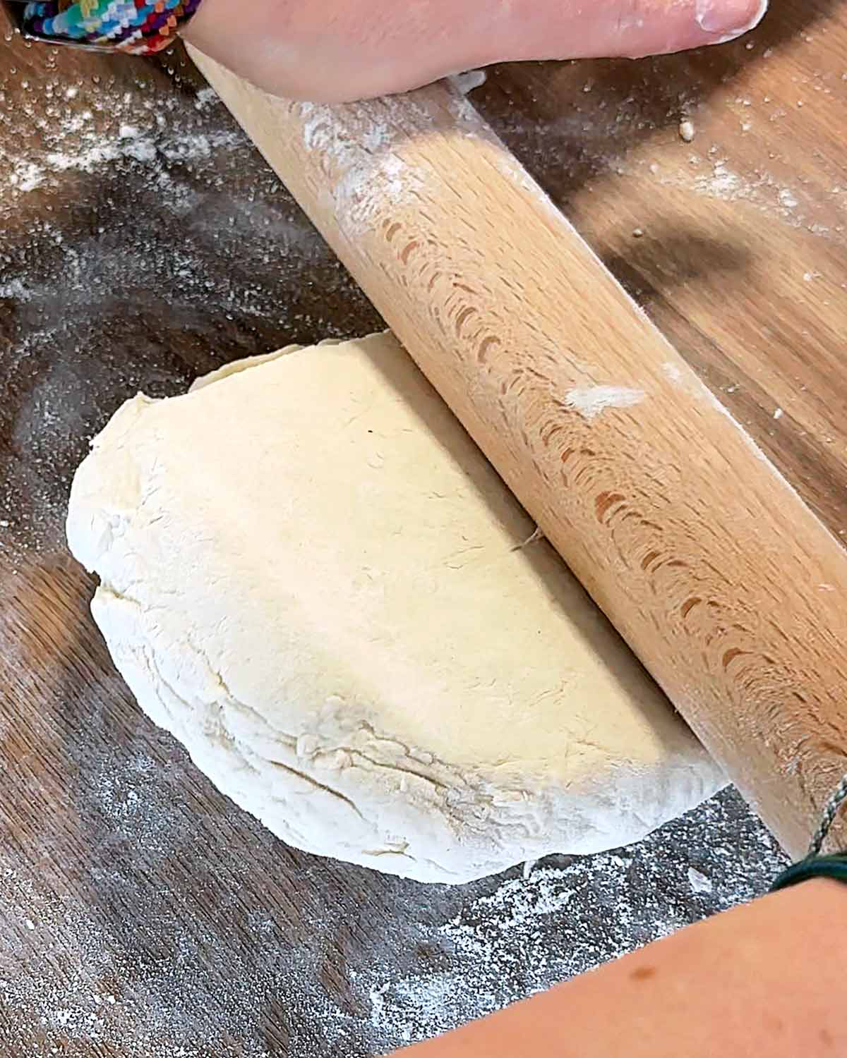 Dough being rolled out on a wooden surface.