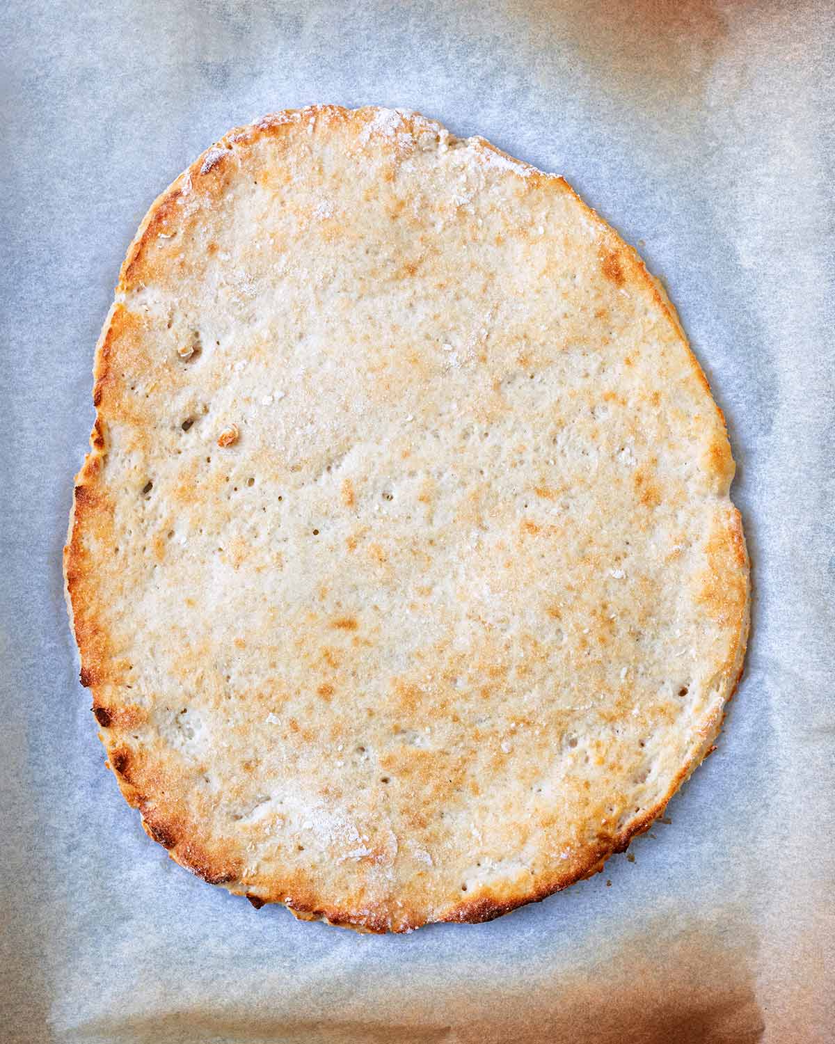 Cooked pizza dough on a lined baking sheet.