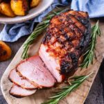 Honey roast ham on a wooden serving board with sprigs of rosemary.