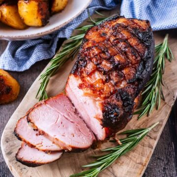 Honey roast ham on a wooden serving board with sprigs of rosemary.