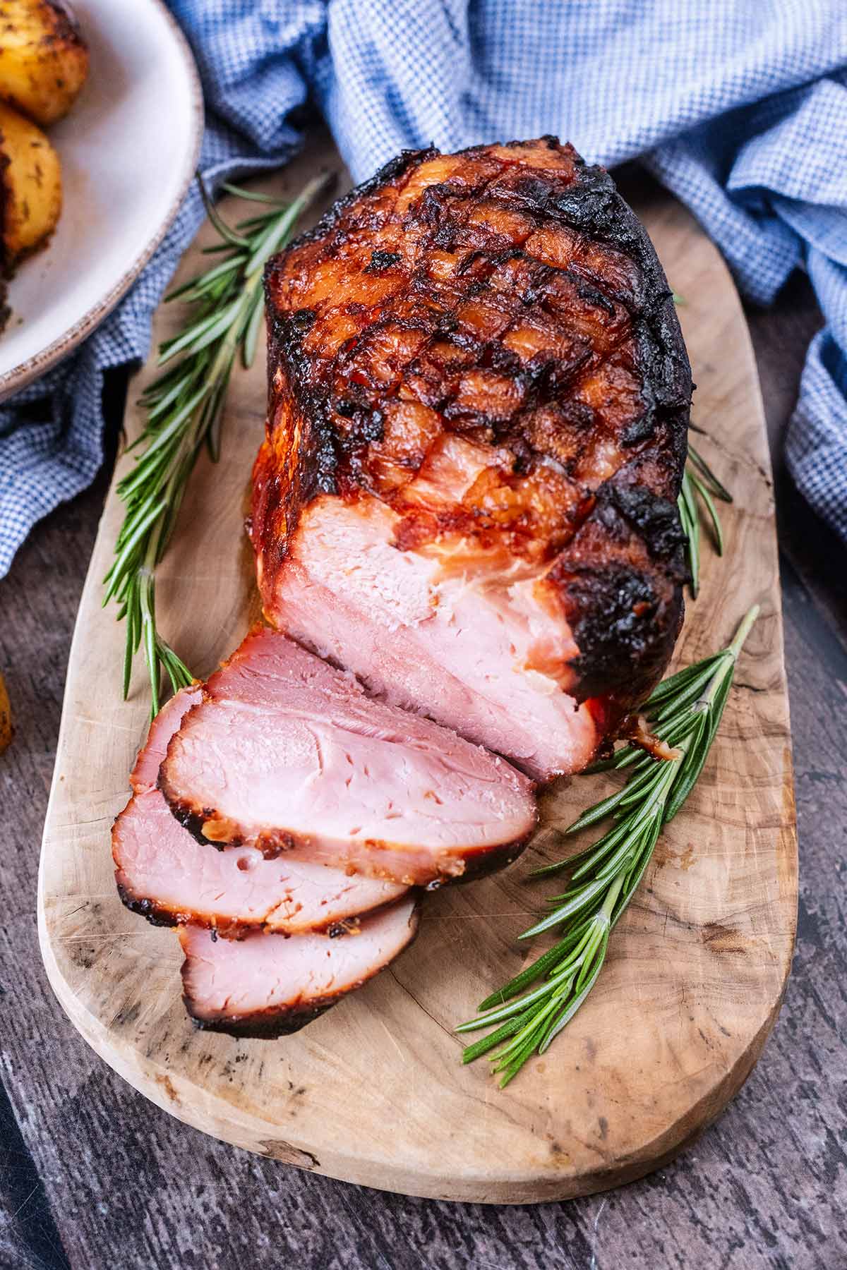 a joint of cooked ham on a wooden serving board with three slices cut off.