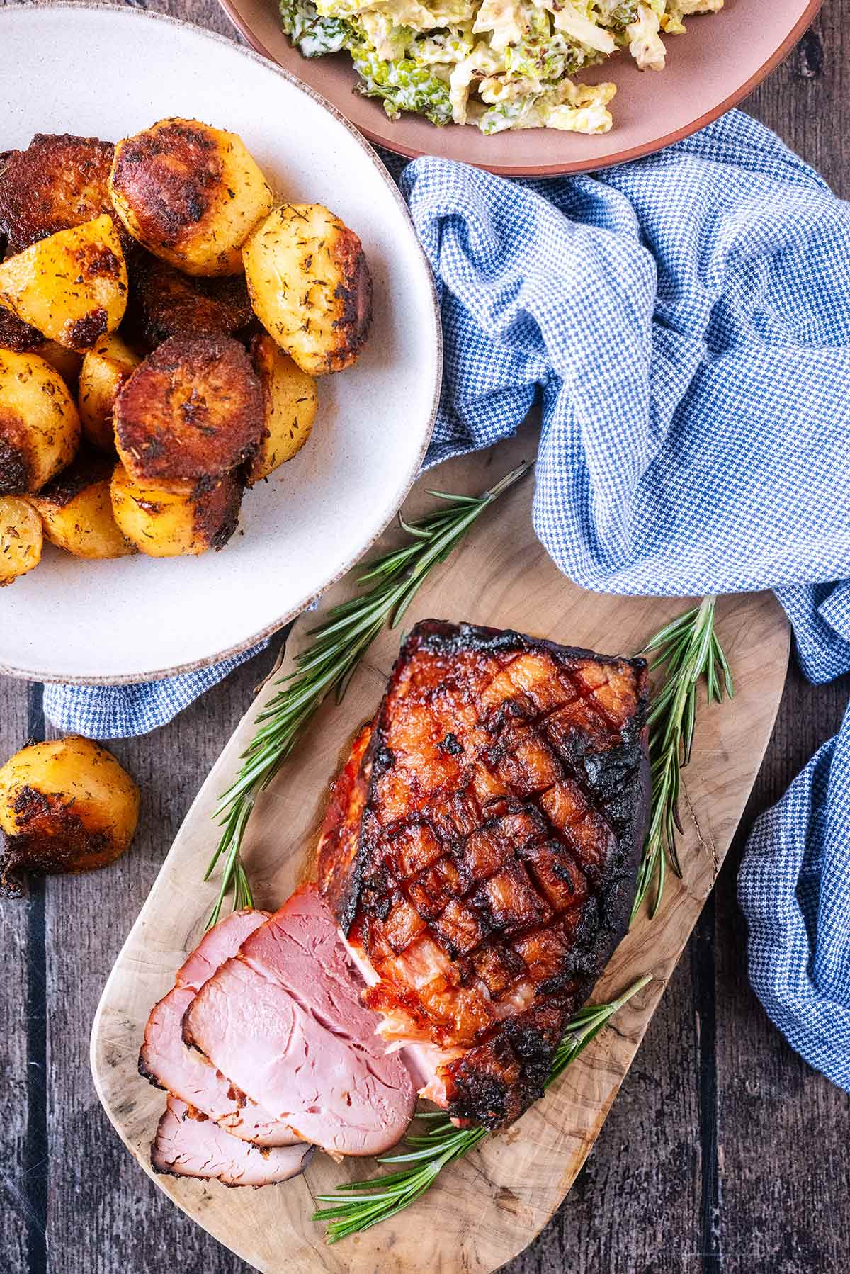 Cooked ham joint next to a bowl of roast potatoes and a bowl of cooked cabbage.