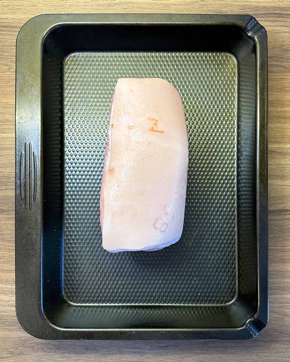 A raw ham joint in a large black baking tray.