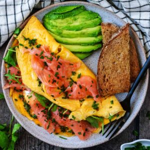 A smoked salmon omelette on a plate with sliced avocado and toast.