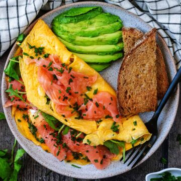 A smoked salmon omelette on a plate with sliced avocado and toast.