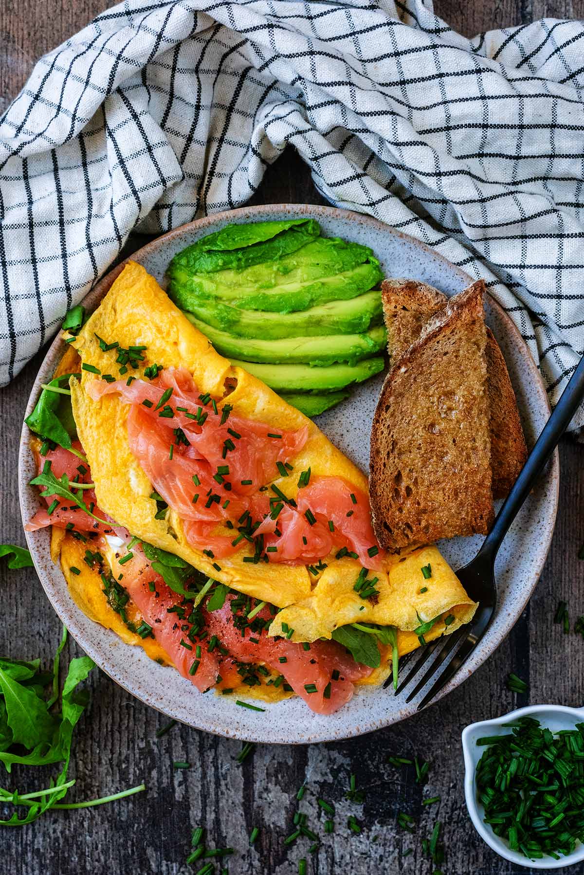 Salmon omelette, avocado and brown toast on a round grey plate.