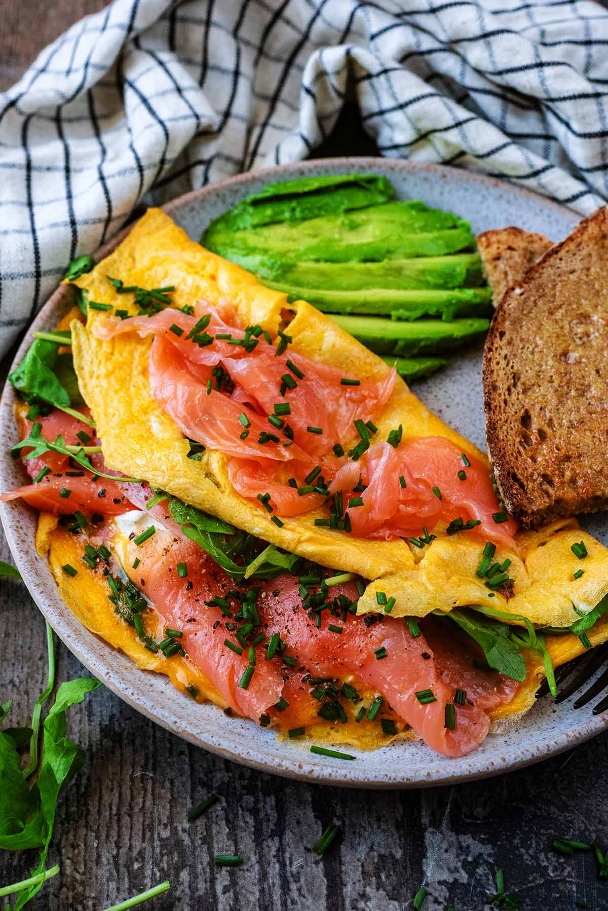 An omelette on a plate with sliced avocado and slices of buttered toast.