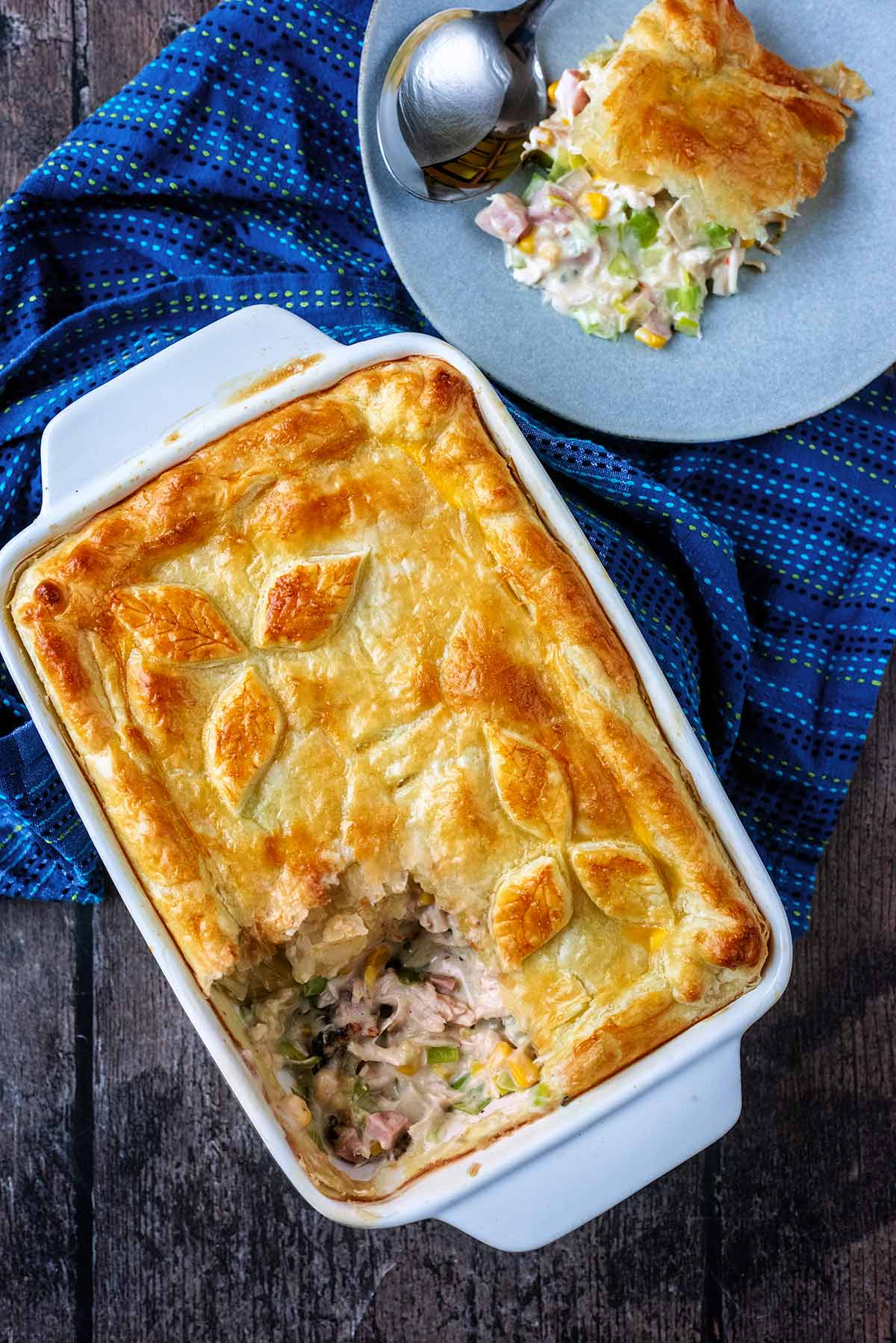 Puff pastry topped pie in a baking dish with a portion removed and put on a plate.