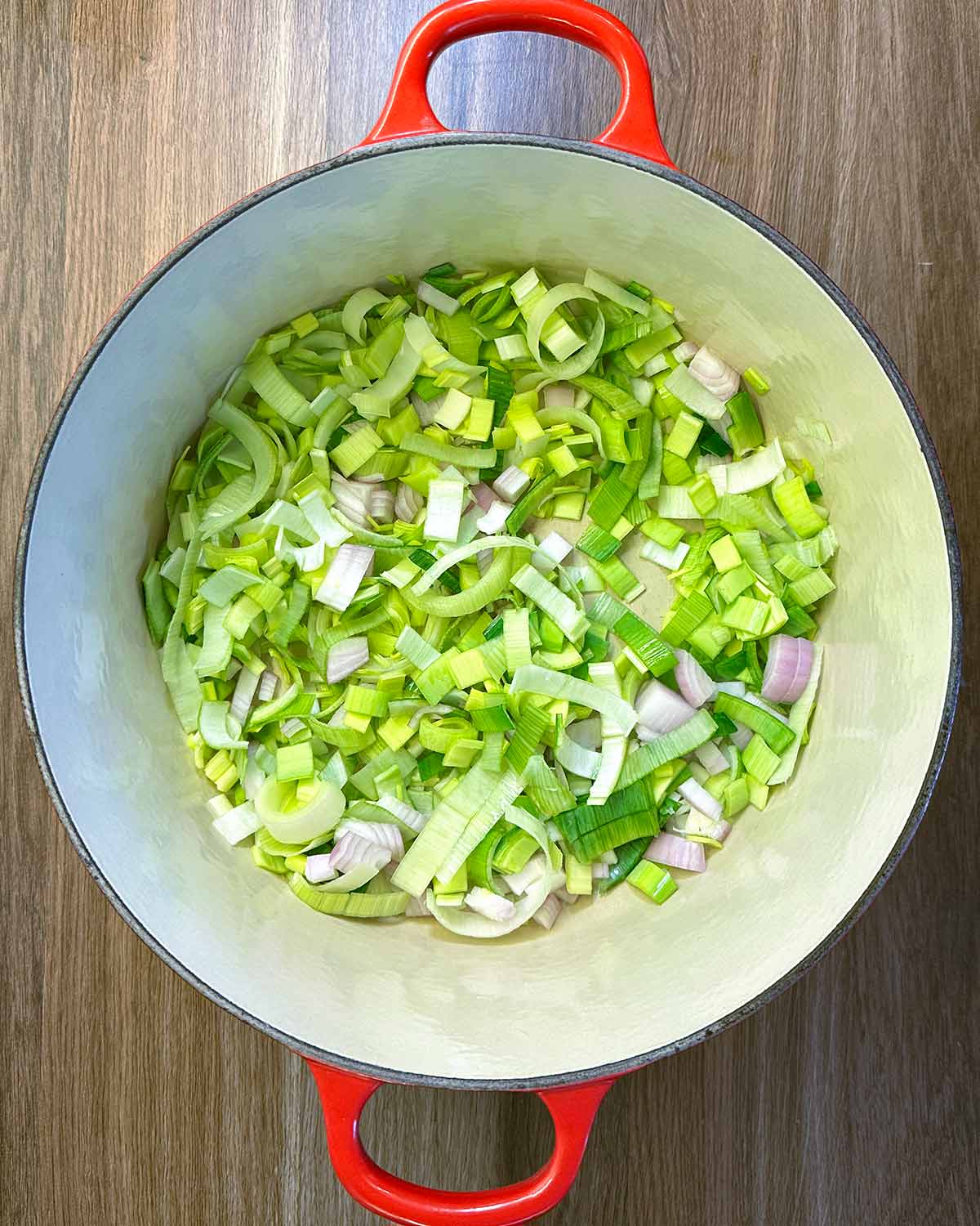 Chopped leeks and onion cooking in a large red pan.