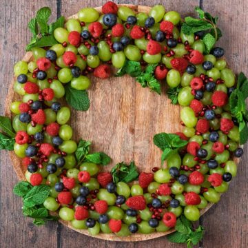 A Christmas Fruit Wreath on a large round wooden board.