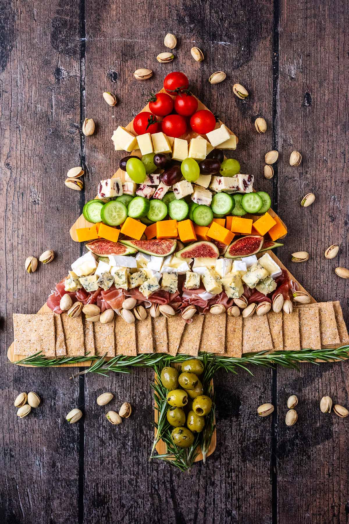 Various cheeses, fruit and crackers on a Christmas tree shaped board.