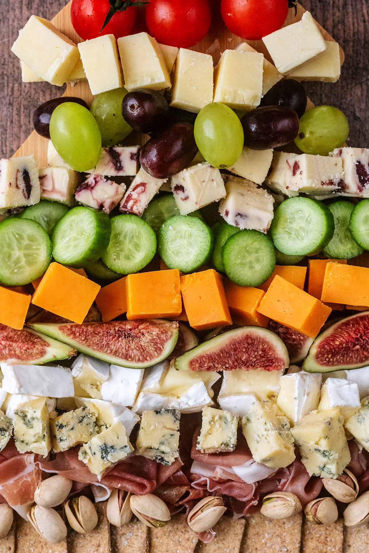 Rows of cheese cubes, grapes, olives, sliced figs, nuts and crackers.