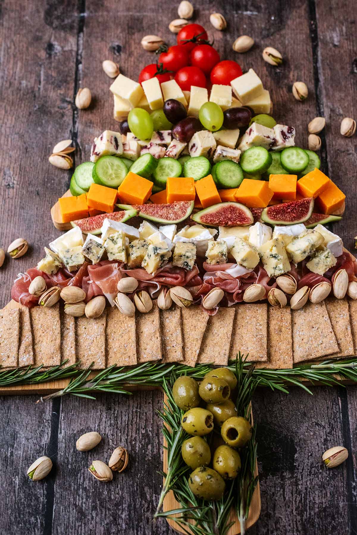 A Christmas tree shaped charcuterie board surrounded by pistachio nuts.