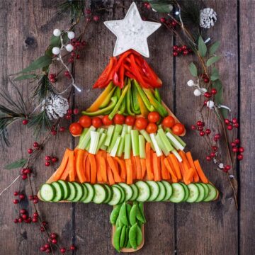 A Christmas Veggie Tray on a wooden surface surrounded by Christmas decorations.