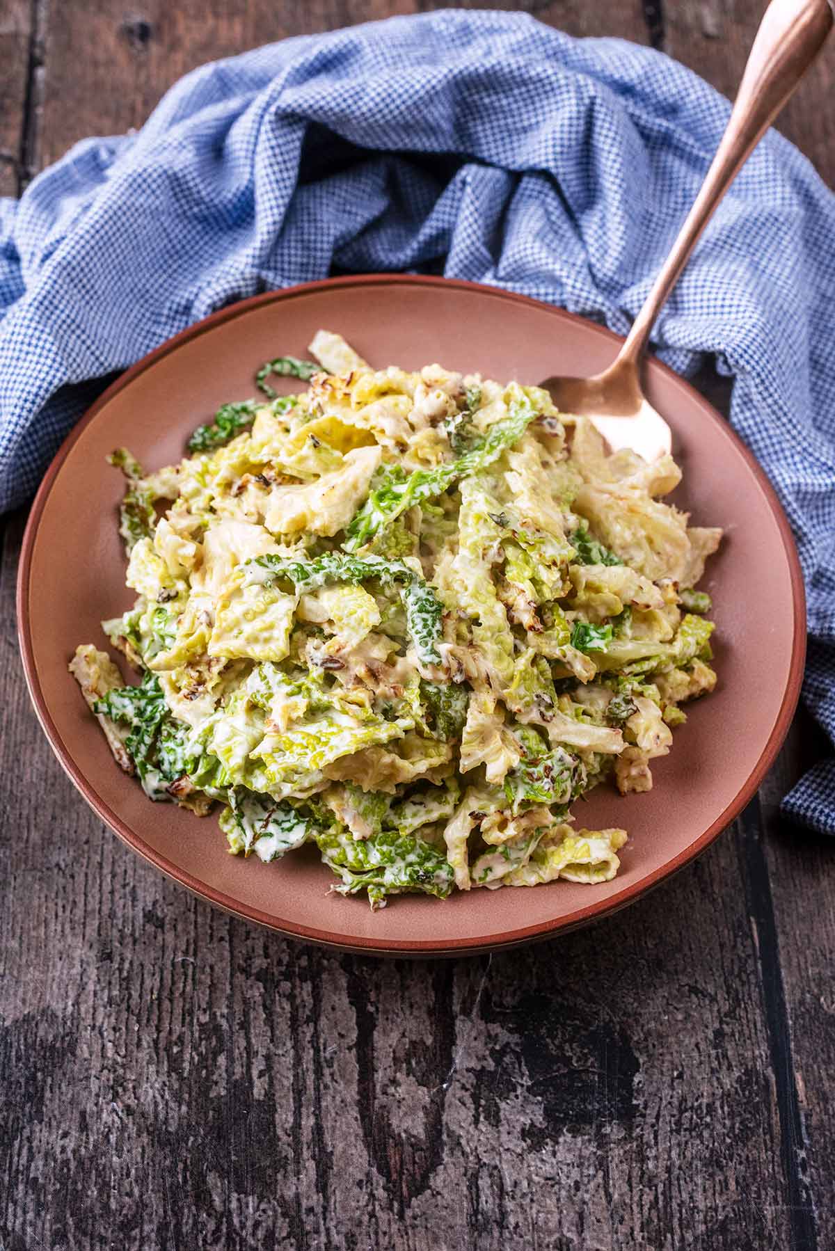 A bowl of cooked cabbage on a wooden surface in front of a blue towel.