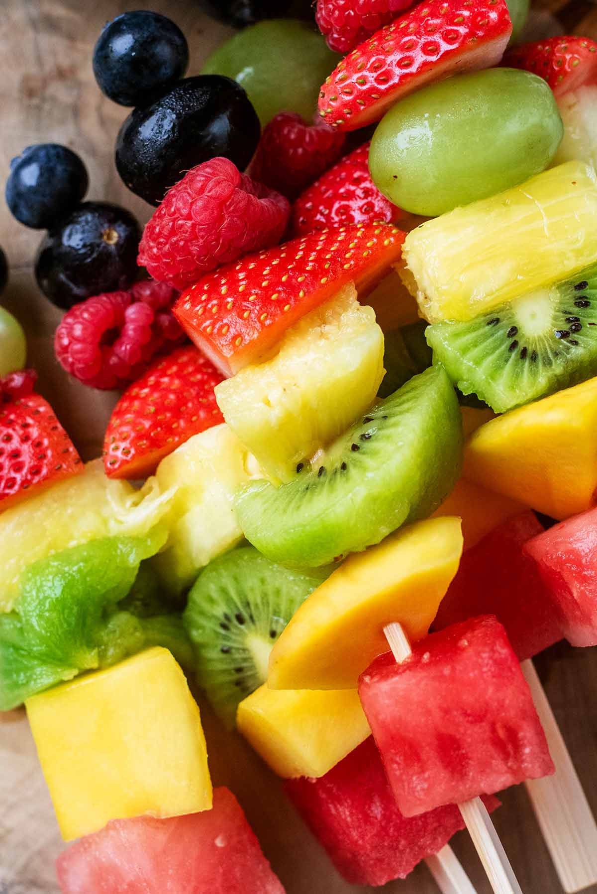 Melon, pineapple, mango, kiwi, strawberry, raspberry, grape and blueberry all pushed onto a wooden skewer.