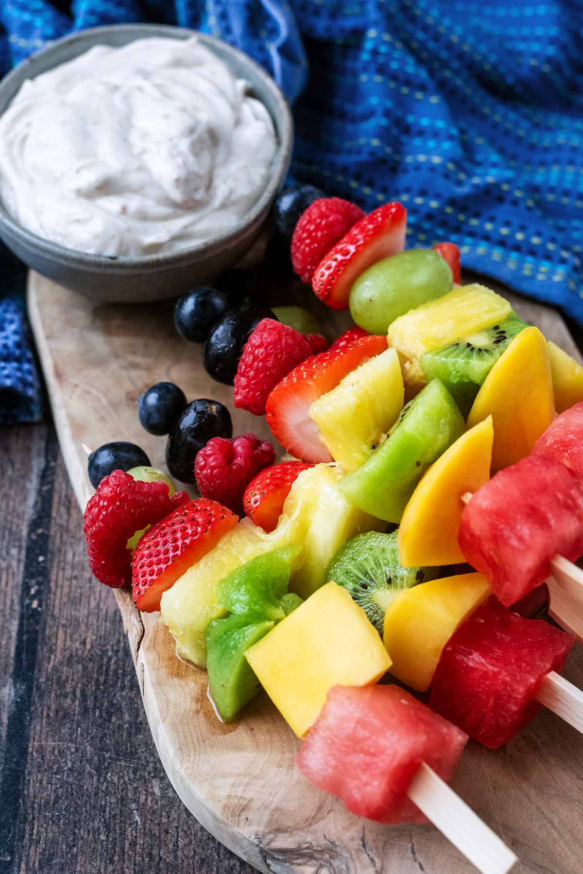 A bowl of creamy dip next to some fruit skewers.