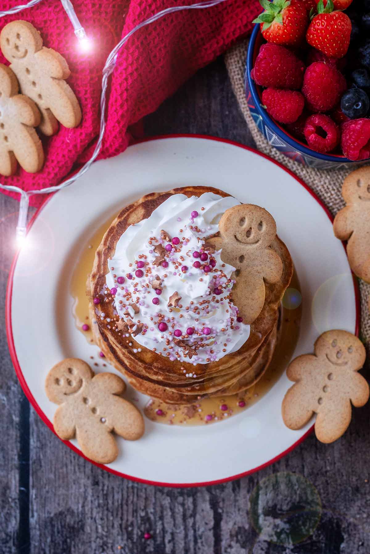 Whipped cream, festice sugar sprinkles and a gingerbread person on top of some pancakes.