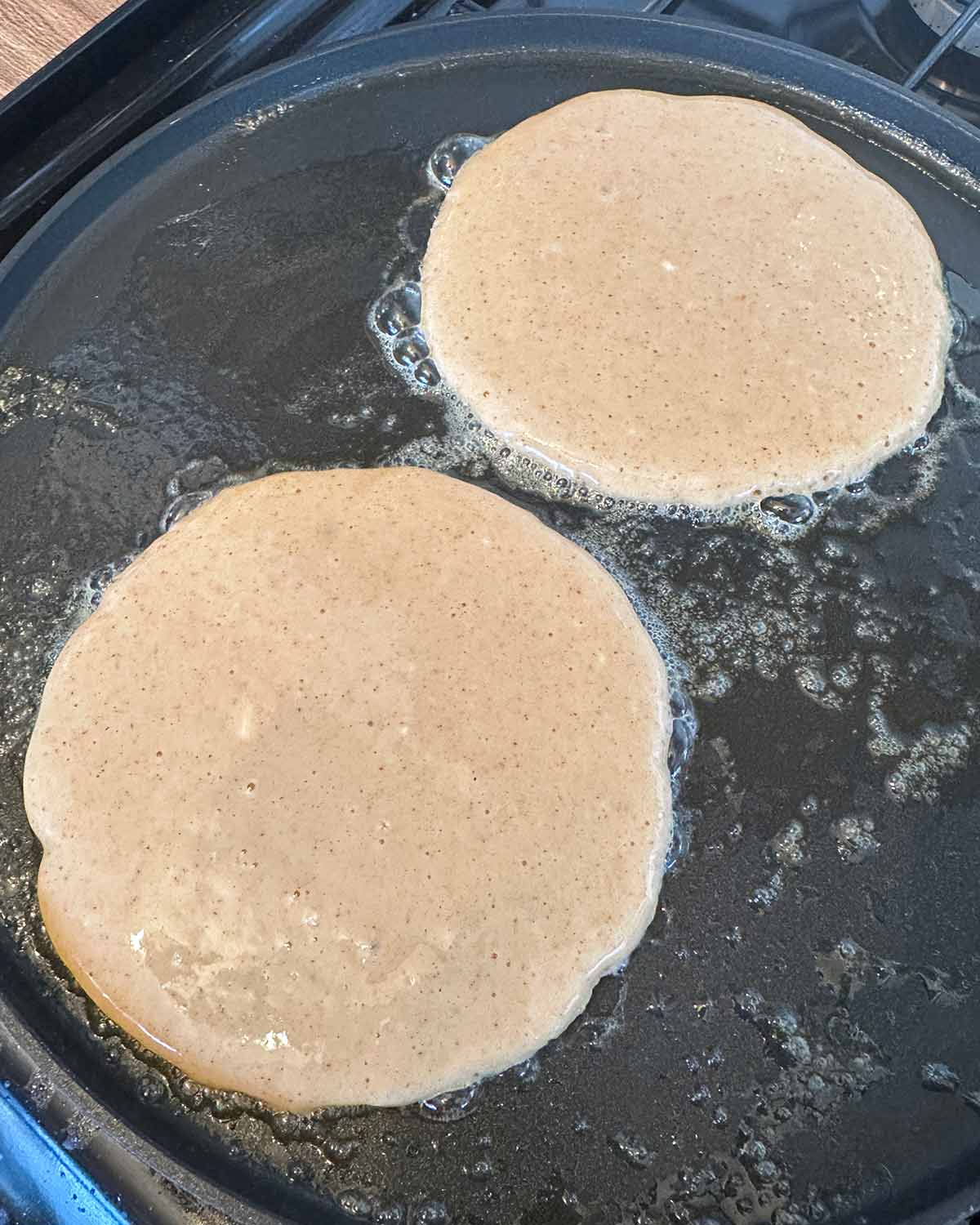 Two pancakes cooking on a flat pan.